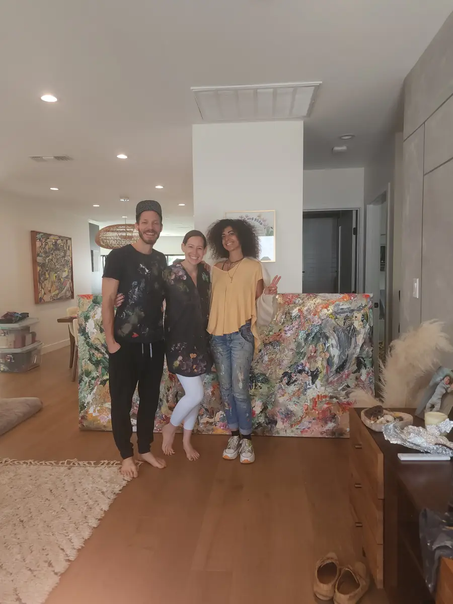 Galeet with two smiling clients in their living room, beside a large colorful painting
