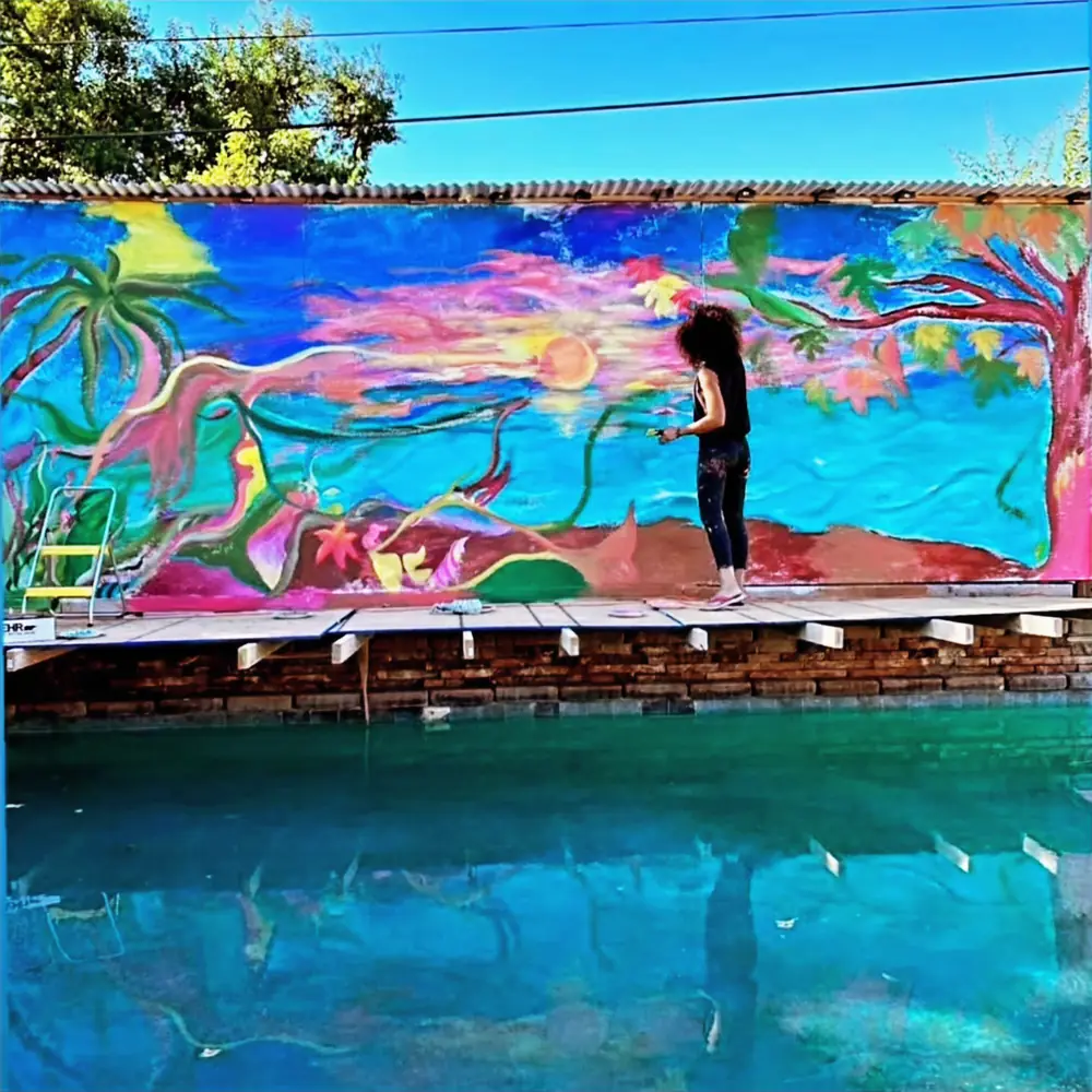 Galeet painting a bright mural of palms and a sunset on a backyard pool wall